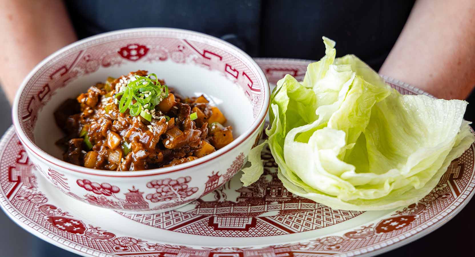 Bowl of minced pork in hoisin sauce with diced vegetables, served with fresh iceberg lettuce leaves.