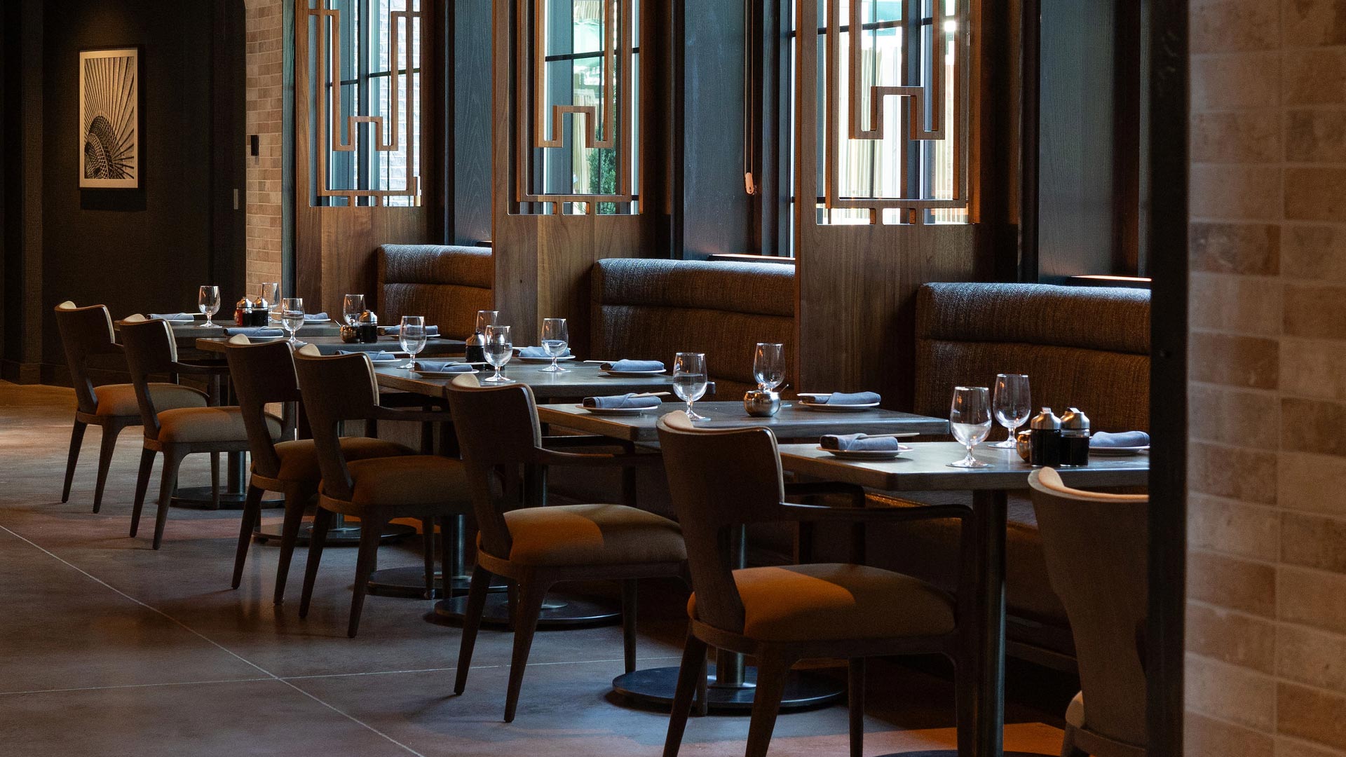 Elegant indoor dining area with wood-accented booths, modern lighting, and neatly set tables with stemware and rolled napkins.