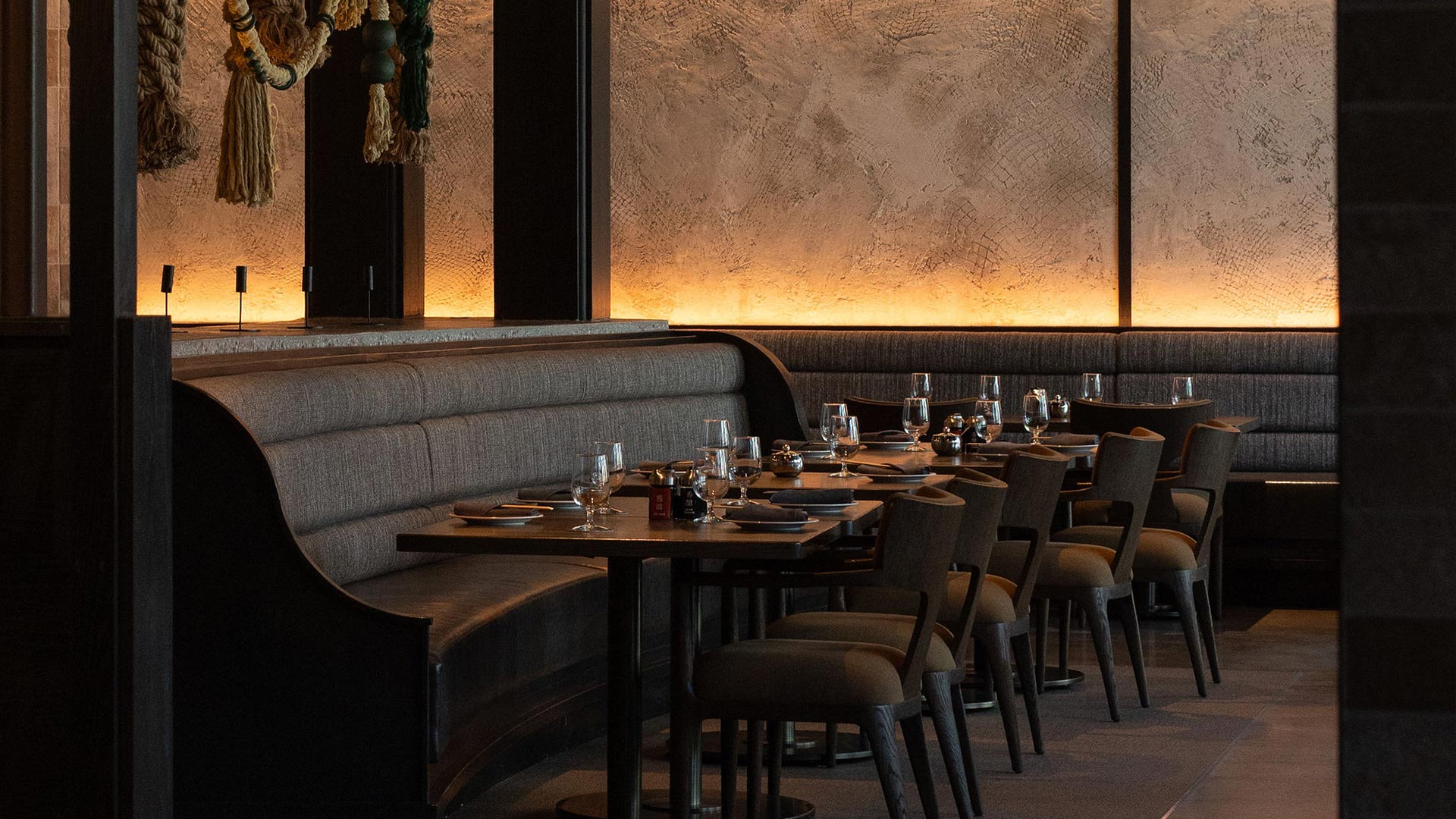 Dimly lit dining room with curved booth seating, textured accent wall, and warm ambient lighting for a cozy, upscale atmosphere.
