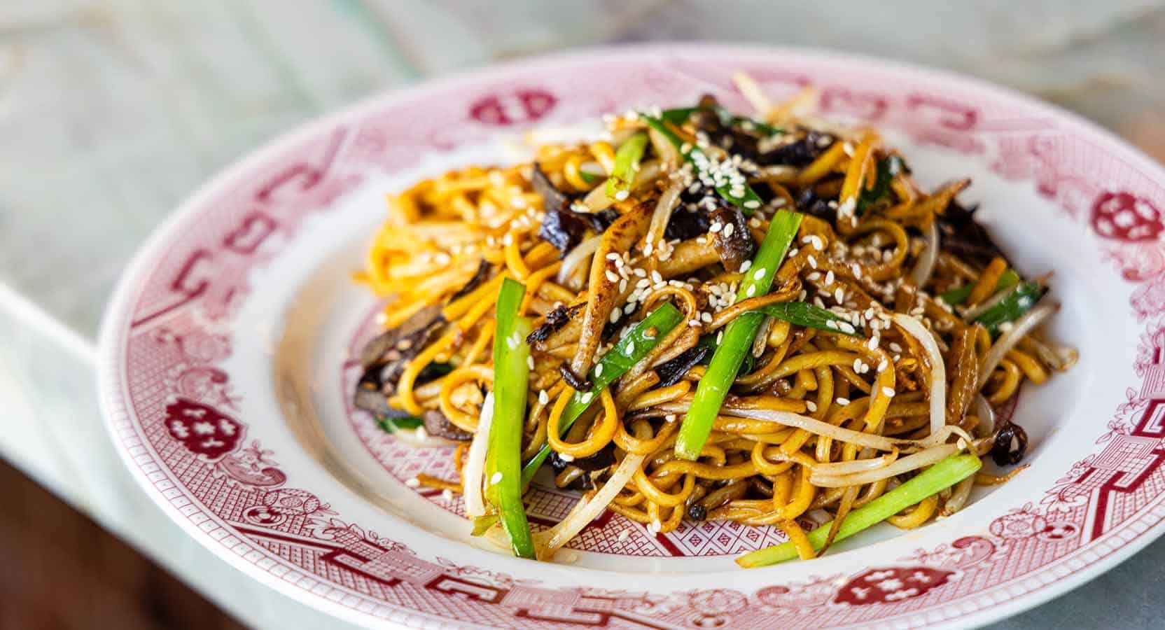 Savory Asian stir-fried noodles with vegetables and sesame seeds, served on a traditional patterned plate.