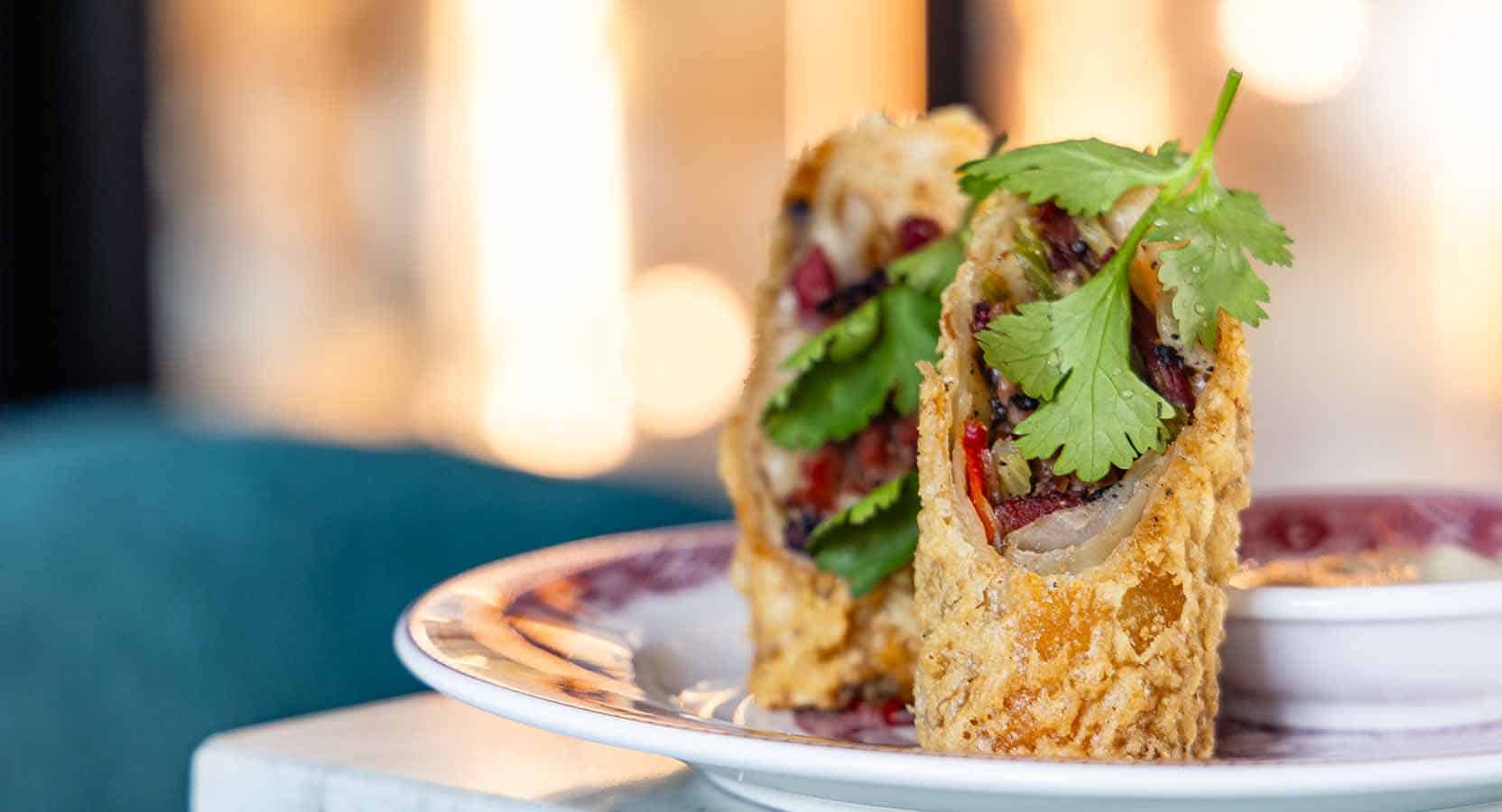 Crispy fried appetizer with fresh herbs and colorful vegetables, served on a decorative plate, highlighting Asian-inspired cuisine and traditional flavors.